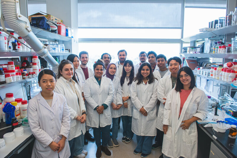 A group photo of additive manufacturing students in a lab wearing white coats
